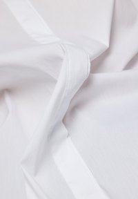 White fabric with a smooth texture, featuring subtle sheen and delicate stitching details. Material appears lightweight and soft.