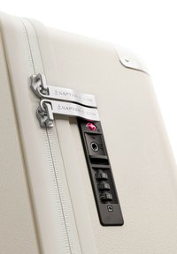 Witte harde koffer met een gestructureerd oppervlak, dubbele metalen ritsen gelabeld "KAPTEN & SON," en een zwart combinatie slotpaneel.