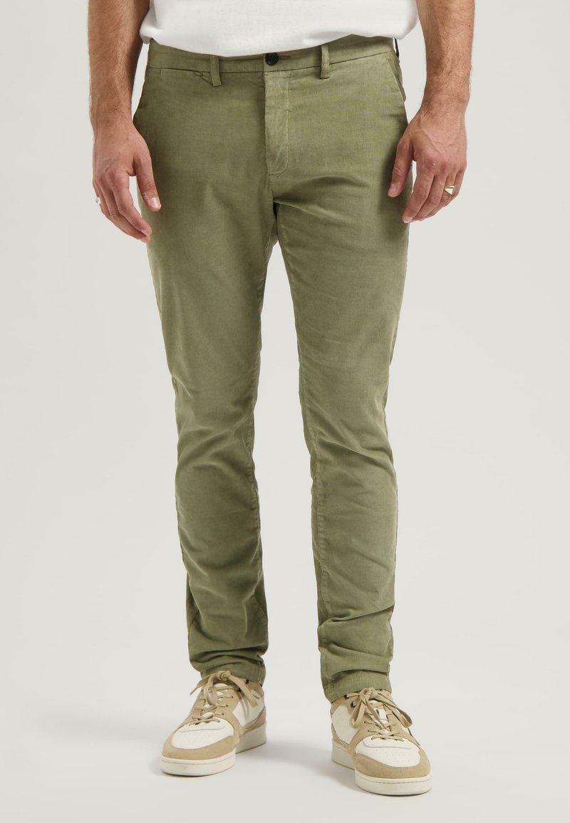 Pantaloni in corda verde oliva con vestibilità slim, dotati di chiusura frontale con bottone e tasche laterali inclinate, abbinati a sneaker beige.