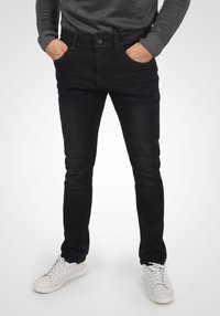 Los jeans de mezclilla negros presentan un ajuste slim, un diseño de cinco bolsillos, un sutil desgastado y se combinan con zapatillas blancas. La textura parece suave.