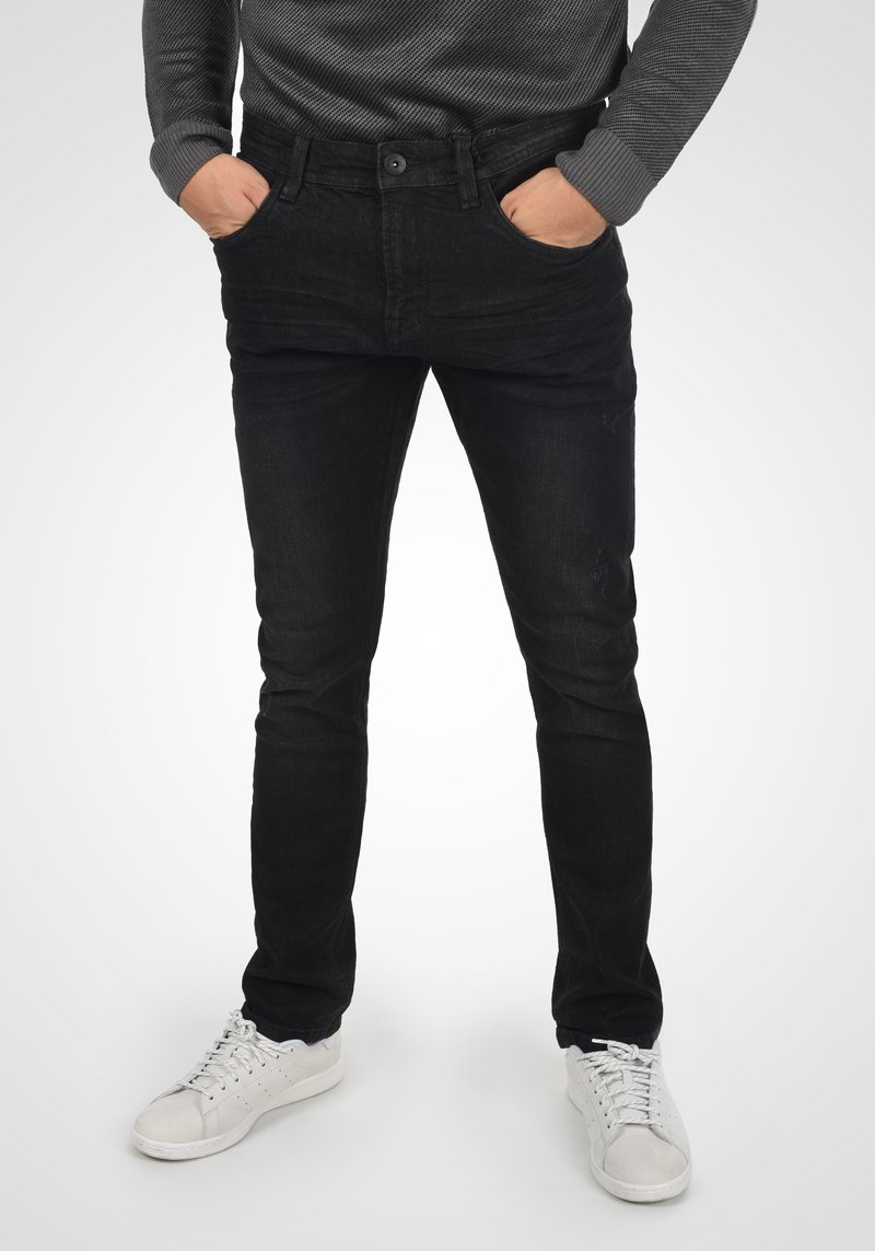 Los jeans de mezclilla negros presentan un ajuste slim, un diseño de cinco bolsillos, un sutil desgastado y se combinan con zapatillas blancas. La textura parece suave.