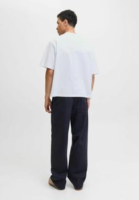 Tricou alb din bumbac cu mâneci scurte, croi lejer și decolteu rotund, combinat cu pantaloni largi de un bleumarin închis. Textură simplă, design minimalist.