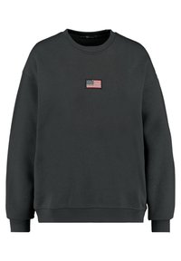 Svart crewneck sweatshirt med långa ärmar, som har en liten broderad amerikansk flagga centrerad på bröstet.