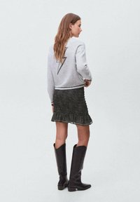 Siva pulover s obliko strele na hrbtu, v kombinaciji s črno cvetlično krilo z volančki in črnimi škornji do kolen.