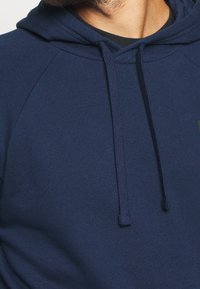 Felpa blu navy con cappuccio regolabile, realizzata in tessuto morbido. Presenta maniche raglan e una tasca a marsupio. Design semplice, senza fantasie.