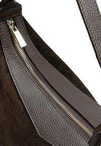 Detailní záběr na část tmavě hnědé strukturované kožené tašky s viditelným zipem a odpovídajícím koženým páskem.