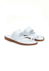 Sandalias planas blancas con una amplia correa y un lazo para el dedo del pie, hechas de material suave con una suela marrón y costuras decorativas a lo largo del borde.