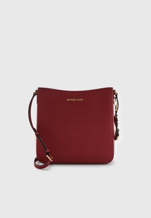 Bordowa skórzana torebka crossbody Michael Kors z regulowanym paskiem i złotymi okuwaniami na jasnoszarym tle.