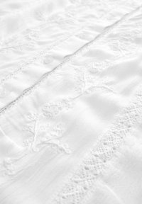 Gros plan d'un tissu blanc avec une fine broderie florale, un bord en dentelle et de petits boutons le long d'une couture.