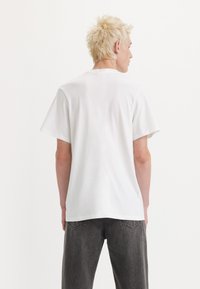 Camiseta de algodón blanca con mangas cortas, cuello redondo y un corte relajado, vista desde la parte de atrás con una textura suave.