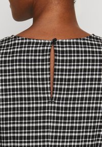 Svartvitt rutigt tyg med knappstängning baktill och en liten nyckelhålöppning. Lättviktsdesign, strukturerad.