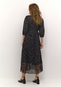 Black and gray leopard print dress with puff sleeves, smocked waist, and pleated skirt. Worn with black block-heeled shoes.