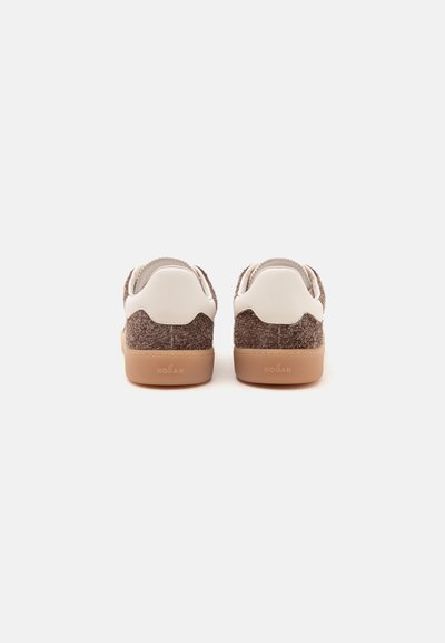 Paire de baskets marron et blanches avec semelles marron clair, vues de dos sur un fond blanc.