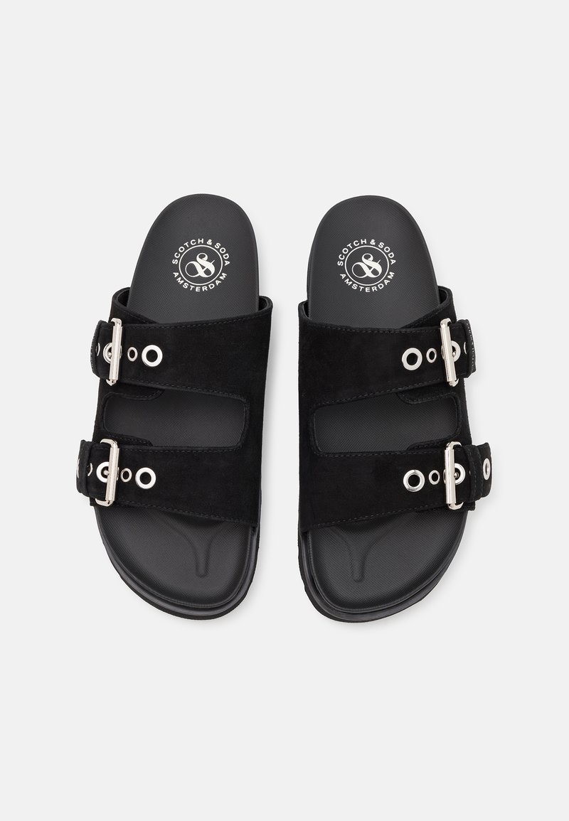 Schwarze Wildledersandalen mit zwei verstellbaren Riemen, die mit silbernem Zubehör und kreisförmigen Ausschnitten auf einer strukturierten schwarzen Sohle versehen sind. Markenlogo sichtbar.