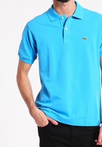 Ljusblå polo skjorta i slät bomull, med klassisk krage, korta ärmar och en grön krokodil-logotyp på bröstet.