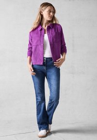 Lilla corduroy-jakke med to forlommer, parret med blå jeans og hvide sneakers. Jakken har en knaplukning og en krave.