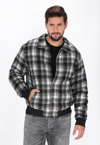 Czarna i biała kurtka w kratę z zapięciem na guziki, z ko�łnierzem, przednimi kieszeniami i ściągaczami przy mankietach. Wykonana z miękkiego materiału, o luźnym kroju.
