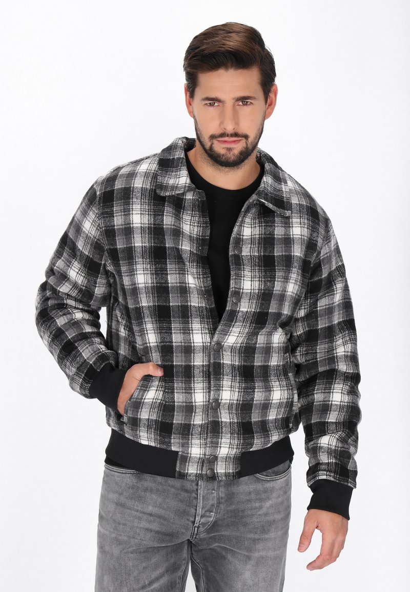 Czarna i biała kurtka w kratę z zapięciem na guziki, z kołnierzem, przednimi kieszeniami i ściągaczami przy mankietach. Wykonana z miękkiego materiału, o luźnym kroju.