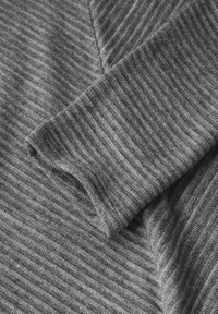 Grauer, gerippter Sweaterstoff, der eine Nahaufnahme des Ärmels zeigt und die weiche Textur sowie die vertikalen Streifen hervorhebt.