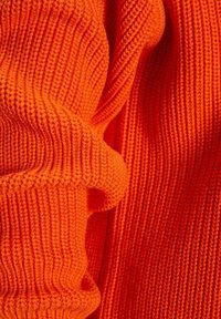Gros plan sur un tissu tricoté orange vif avec une texture côtelée et des plis créant des ombres et de la profondeur.