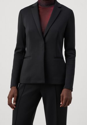 Black tailored blazer in lightweight fabric, single-button design, notch lapels, and two front pockets, paired with a dark top.