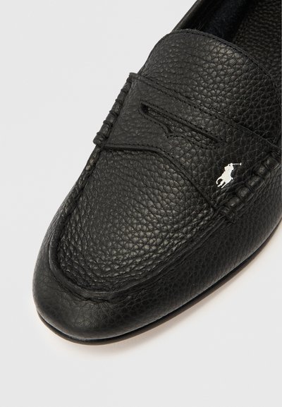 Mustast nahast mokassiin, millel on tekstuuriga pind, õmmeldud aktsendid ja valge logo. Ümar ninaga ja libisev tallaga disain.
