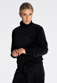 Czarny ażurowy golf z długimi rękawami i marszczonymi mankietami, o gładkiej teksturze i luźnym kroju. Idealny na codzienne wyjścia.