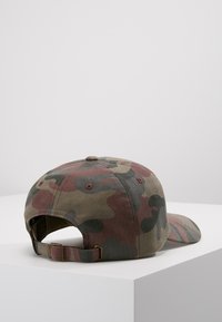 Cappello da baseball in camouflage con una combinazione di tonalità di verde e marrone, fascia regolabile sul retro, realizzato in tessuto con una superficie leggermente strutturata.