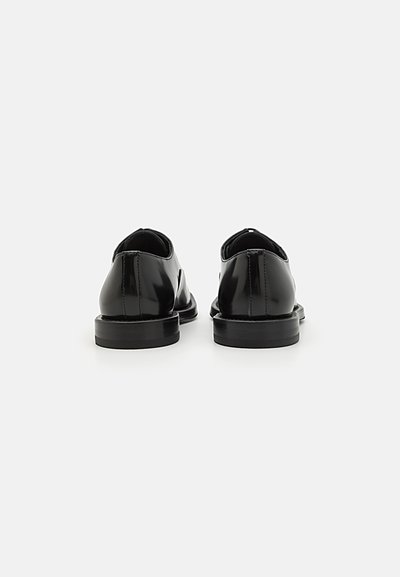Black patent leather shoes with a low heel, rounded toe, and minimal stitching. Features a sleek, smooth texture and a simple design.