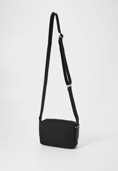 Sac à bandoulière noir de forme rectangulaire, avec fermeture éclair, en tissu texturé et avec une sangle réglable. Doté d'une finition lisse et mate.