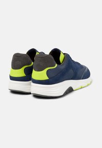 Scarpe sportive blu e grigie con dettagli verdi e suola bianca, mostrate da dietro, evidenziando il loro design moderno e il contrasto di colori.