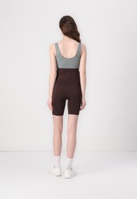 Fitted gray tank top with wide straps paired with high-waisted brown shorts, featuring a smooth texture and a knee-length cut, worn with white shoes.