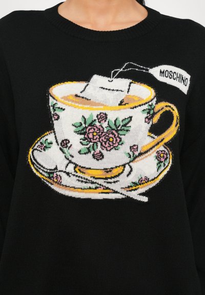 Schwarzer Pullover mit einem Design von Teetasse und Untertasse. Die Tasse hat florale Muster, einen Teebeutel und ein "Moschino"-Etikett auf weißem Hintergrund.