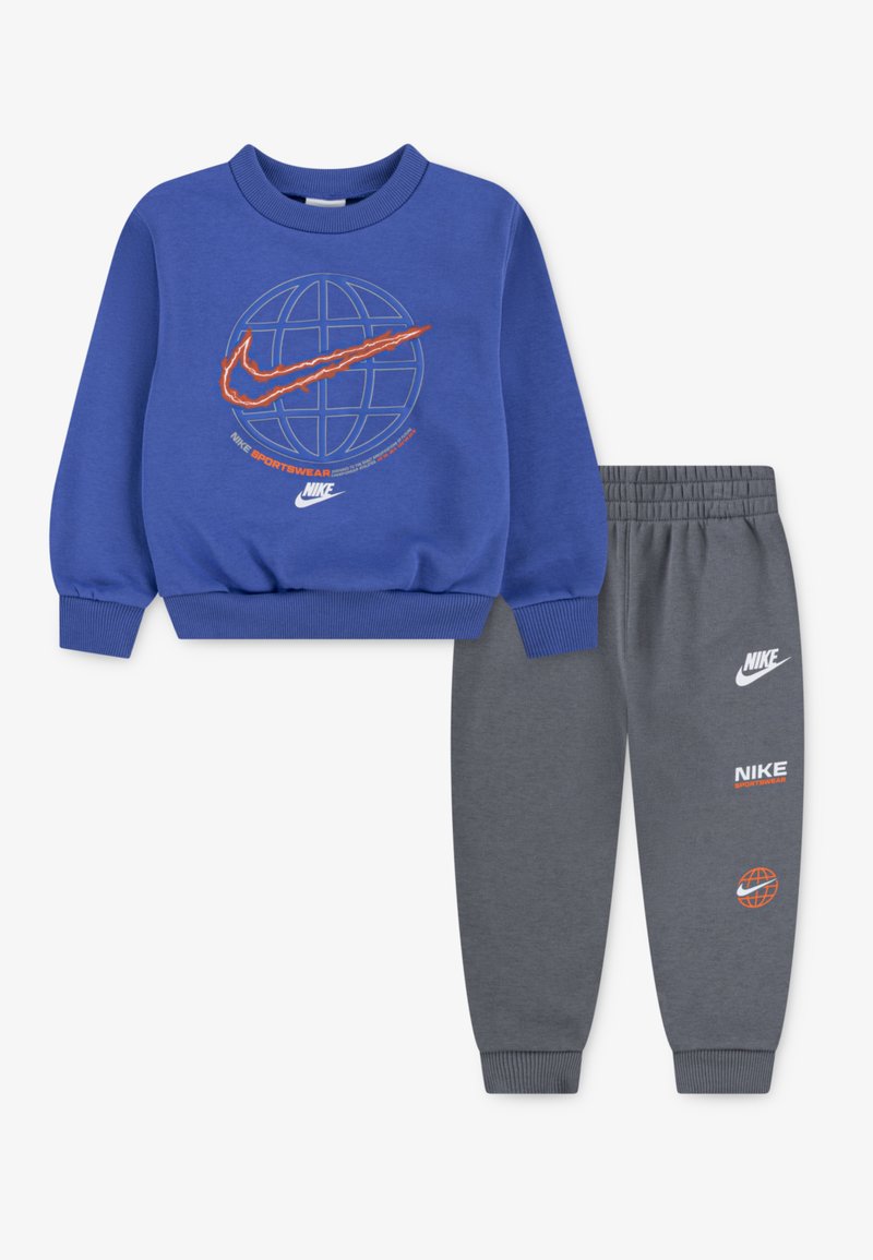 Conjunto de duas peças da Nike com um sweatshirt azul com um gráfico de globo e pormenores laranja, combinado com calças de moletom cinzentas com detalhes do logo.