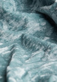 Un tissu doux et texturé dans une couleur bleu sarcelle atténuée, avec un léger éclat et des motifs de vagues subtils, créant une apparence luxueuse.