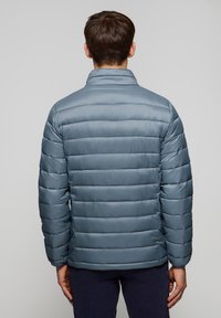 Vadderad jacka i ljusblått, med horisontell quiltad textur, hög krage och en slät, blank yta. Normal passform.