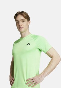 Groene sportieve T-shirt met korte mouwen, ronde hals, structuurstof, voorzien van een zwart logo op de borst en een slank ontwerp.