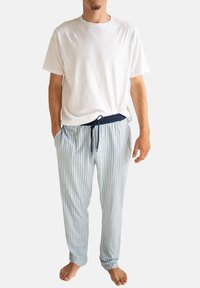 Witte katoenen T-shirt gecombineerd met lichtblauwe gestreepte pyjamabroek met een marineblauwe tailleband met trekkoord. Blootsvoets gedragen.