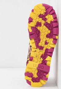 Semelle d’une basket avec des crampons profonds jaune et violet, comportant des motifs circulaires antidérapants et le logo « Liu Jo » sur fond blanc.