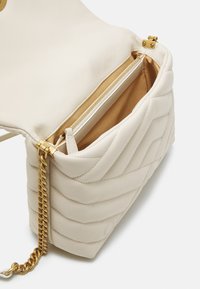 Borsa a tracolla in pelle bianca con texture trapuntata, hardware dorato e scomparto con zip. Presenta una tracolla a catena e una fodera interna liscia.