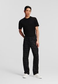 Tricou negru cu maneci scurte și un logo subtil, asortat cu pantaloni negri cu un imprimeu grafic întunecat și adidași albi.