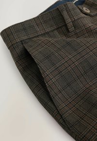 Brune og sorte ternede bukser med en tekstureret vævning, der har en talje og en sidelomme. Stoffet har et struktureret udseende.