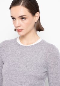 Maglione grigio lavorato a maglia con scollo rotondo, caratterizzato da un bordo a costine contrastante color avorio. Morbida trama, maniche a metà gomito.