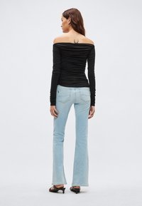 Zwart off-shoulder top met gerimpelde textuur gecombineerd met lichtblauwe wijde jeans. De jeans heeft achterzakken en een subtiel gespleten detail.