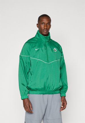 Grüne Windjacke mit hohem Kragen, elastischen Bündchen und Saum. Mit einem weißen Streifen und Logo auf der linken Brust. Leichtes, glänzendes Material.