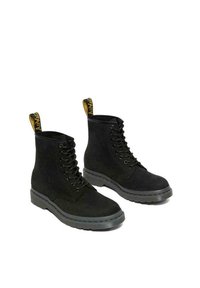 Stivaletti neri in suede con design allacciato, dotati di una suola in gomma grigia e di una linguetta gialla sul tallone. Superficie superiore testurizzata.