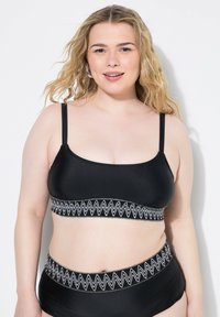 Top da nuoto nero con spalline regolabili, caratterizzato da un cinturino testurizzato a zigzag bianco. Il bottom a vita alta coordinato presenta un design simile.