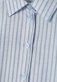 Camisa de rayas azul claro con líneas verticales negras, cuello con botones y botones blancos. La textura parece suave y ligeramente brillante.