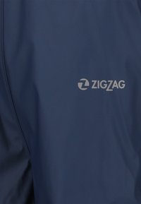 Marinblått vattentätt jacka med "ZIGZAG"-logotypen i silver. Slät textur och enkel design utan synliga mönster.