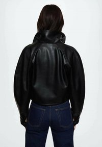 Czarna skórzana kurtka z wysokim kołnierzem i bufiastymi rękawami, z gładką, błyszczącą fakturą i dopasowanym tyłem, w połączeniu z ciemnymi dżinsami.